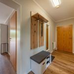 Flur mit Holztür, Garderobe und Sitzbank. Durchgang zu Wohnbereich mit Terrasse.