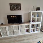 TV auf Holzregal mit Aufbewahrungsboxen und Bücherregal daneben.