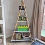 Dreieckiger Holzregal mit Büchern, Spielzeug und Spielboxen im Raum.