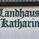 Schild Landhaus Katharina an weißer Ziegelwand unter Dach