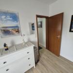 Eingangsbereich mit Schrank, Wandbildern und Tür zum Flur.