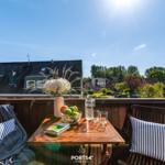 Terrasse mit Tisch, Stühlen und Blumen. Blick auf Häuser und Bäume unter blauem Himmel.
