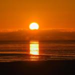 Sunset over the sea with orange sky and reflective water surface.