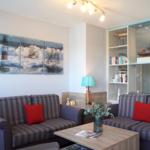 Wohnzimmer mit zwei Sofa, Tisch und Wandbildern mit Schiffen und Leuchtturm.
