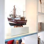 Ein hölzernes Schiffmodell mit dem Namen CUX87 steht auf einem weißen Sockel in einer Glasvitrine.