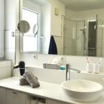 Badezimmer mit Waschtisch, Spiegel und Dusche. Fenster, Handtuch und Haartrockner sichtbar.