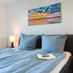 Schlafzimmer mit Bett, zwei Nachttischen und Wandbild. Auf Bett liegt Buch mit Brille.