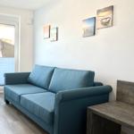 Ein Wohnzimmer mit blauem Sofa, Holzboden und Wandbildern an der Wand.