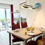 Dining room with table, chairs, and view to balcony. Wall clock and lamp visible.