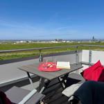 Terrace with table, chairs, and view of grassland and sea.
