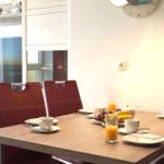 Dining table with four chairs, fruit, and drinks. Wall clock and window in background.