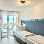 Room with view of balcony and beach. Bed with white bedding and wall with beach motif.