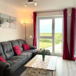 Living room with sofa, table, and view of green field. Red curtains and wall art.