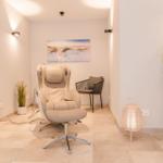 Raum mit Massagestuhl, kleiner Sessel, Pflanzen und Wandbild.