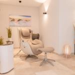 Massagestuhl mit Fußstütze, Wandbild, Pflanzen und Beleuchtung.