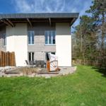 Moderne Villa mit Terrasse und Garten. Holzgeländer und Bäume umgeben das Haus.