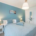 Schlafzimmer mit Bett, Nachttischen und Kleiderschrank. Wand in Blau, Deckenleuchte und Bilder.