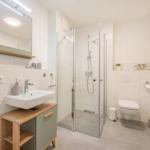 Badezimmer mit Dusche, Waschbecken und Toilette. Moderne Einrichtung mit Holz- und Metallakzenten.