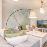 Wohnzimmer mit Sofa, Fernseher und Wandbild. Tisch mit Blumenvase und Gläsern.