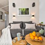 Ein Wohnzimmer mit grauem Sofa, Holztisch und Obst. Wandbild und Lautsprecher sind sichtbar.