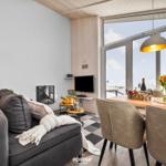 Wohn- und Essbereich mit Sofa, Esstisch und großem Fenster. Holzdecke und Wandverkleidung.