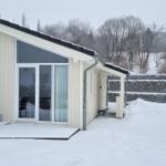 Wohnhaus mit Schneebedeckter Terrasse und Glasfront. Hintergrund: schneebedeckte Bäume und Steinmauer.