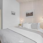 Schlafzimmer mit Bett, Kleiderschrank und Holzwand. Zwei Nachttische mit Pflanzen.