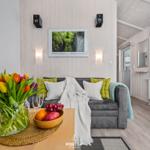 Wohnzimmer mit Sofa, Blumen und Obst auf Tisch. Holzwand und Fenster sichtbar.