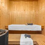 Sauna mit Holzwand, Liegefläche und Steinofen. Handtücher und Bürsten bereit.