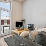 Wohnzimmer mit Sofa, Fernseher und Kamin. Durchgehende Glasfront zum verschneiten Außenbereich.