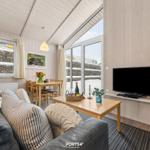 Wohnzimmer mit Sofa, Esstisch und Fernseher. Große Fenster mit Blick auf Steinmauer.