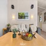 Esstisch mit Obstkorb, Sofa und Wandbild in einem Raum mit Holzwänden.