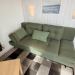 Grünes Sofa mit Kissen, gemusterter Teppich und Wandbeleuchtung im Wohnbereich.