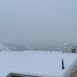 Schneebedeckter Dachfirst mit Blick auf verschneite Berge und Nebel.