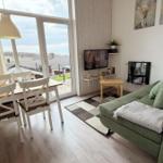 Wohn- und Essbereich mit grünem Sofa, Tisch mit Stühlen und Balkon mit Blick.