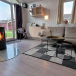 Wohnzimmer mit Kamin, Sofa, Tisch und Fenster. Holzdielen und Teppichboden.