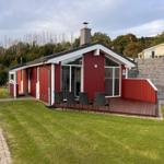 Rotes Ferienhaus mit Terrasse und Garten. Vier Stühle stehen auf der Terrasse.