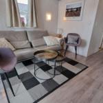 Wohnzimmer mit Sofa, zwei Sesseln, Tisch und Teppich. Durchgang zur Schlafzimmer.