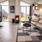 Wohnzimmer mit Kamin, Sofa und TV. Durchgänge zu einer Terrasse und Garten.