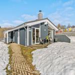 Moderne Ferienhaus mit Terrasse, Schnee und Holzweg. Glastüren und graue Fassade.