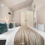 Schlafzimmer mit Bett, Kleiderschrank und Fenster. Holzwand und Decke.