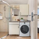 Badezimmer mit Dusche, Waschmaschine und Spiegel. Blick in Schlafzimmer mit Bett.