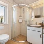 Badezimmer mit Dusche, Waschbecken und Toilette. Holzdecke und Fliesenboden.