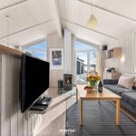 Wohnzimmer mit Sofa, Couchtisch und Fernseher. Holzwände und große Fenster.