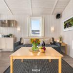 Wohnzimmer mit Sofa, Tisch und Fenster. Holzwände und -decke. Blumen und Obst auf dem Tisch.