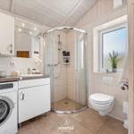 Badezimmer mit Dusche, Waschmaschine und Toilette. Fenster mit Pflanze.