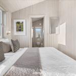 Schlafzimmer mit Holzwand, Bett, Fenster und angrenzender Toilette.