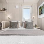 Schlafzimmer mit Bett, Fenster und Wandbild. Holzwände und dekorative Kissen.