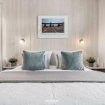 Schlafzimmer mit Bett, Wandbild und Nachttischen. Badezimmer im Hintergrund.