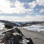 Schneebedeckter Weg mit Steinmauer und Blick auf bewaldete Hügel und Ferienhaus.